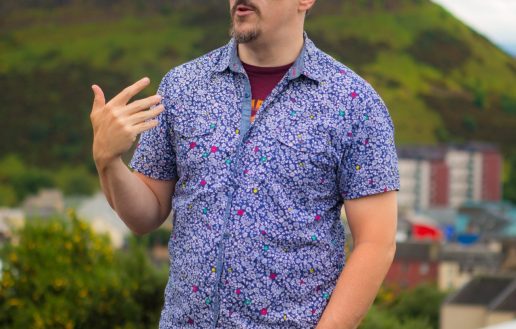 Paddy wearing a patterned shirt atop Calton Hill with a view of the crags in the background